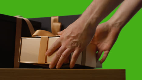 Close-Up-Of-Man-Picking-Up-Gift-Wrapped-Presents-In-Boxes-Decorated-With-Ribbon-On-Table-Shot-Against-Green-Screen-2